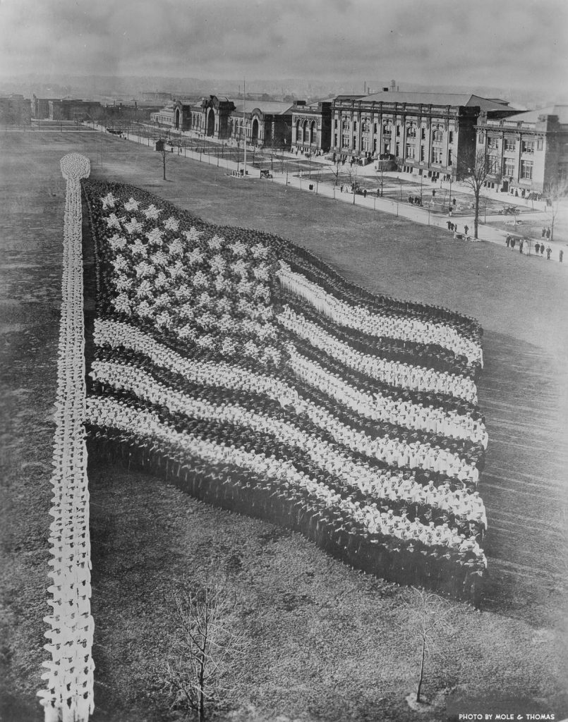 Living photograph of an American flag comprised of 10,000 recruits at the Great Lakes Naval Training Station, Illinois, June 11, 1917. Width of left side of the flag: 428 feet; width of the right side of the flag: 128 feet; length of top of the flag: 293 feet; length of bottom of the flag: 73 feet; width of left end of star field: 350 feet; width of right end of star field: 184 feet; length of top of star field: 143 feet; length of bottom of star field: 66 feet. 700 men were used to form the flagpole. The star on the lower right side used twelve men, while the star on the upper right side required sixty-five. (Photo by Arthur S Mole & John D Thomas/Chicago History Museum/Getty Images)