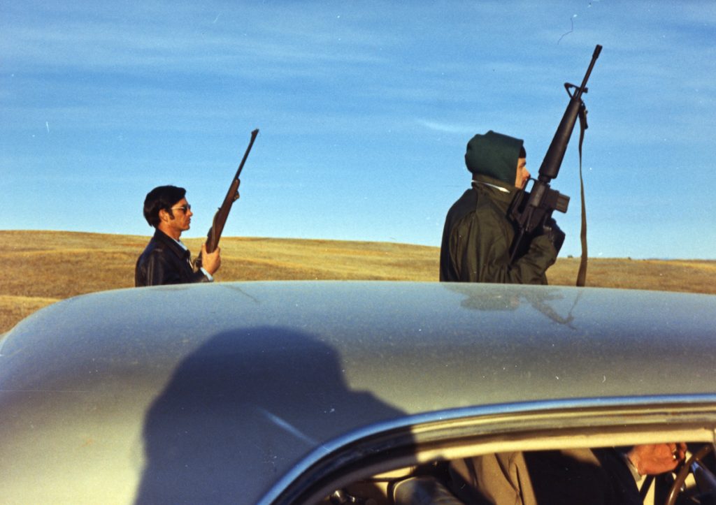 View, over the roof of a car, of a pair of armed Federal Marshals as they stand guard at an Federal Bureau of Investigation (FBI) roadblock during the American Indian Movement (AIM) occupation of the town of Wounded Knee on the Pine Ridge Reservation, South Dakota, 1973. AIM occupied the town, exchanging gunfire with local and federal troops, from February 27 through May 8, 1973, following internal reservation disputes as well as disatisfaction with the US government's treatment of Native American peoples in general. (Photo by Peter Davis/Getty Images)